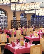 Restaurante elegante con mesas de manteles rosas, sillas de madera y lámparas colgantes.