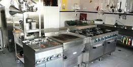 Professional kitchen with stoves, steel counters, and hanging utensils.