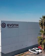 Edificio de Evonik con palmera y coches estacionados bajo un cielo despejado.