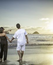 Pareja camina de la mano en la playa al atardecer, mirando el sol y el mar.