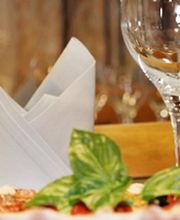 Pizza mit Basilikum, Weingläsern und Servietten in einem Restauranttisch-Arrangement.