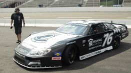 Race car number 76 on a track, with a person nearby, featuring brand logos.