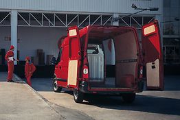 Roter Lieferwagen mit offenen Türen, drei Personen in roten Uniformen an der Seite eines Gebäudes.