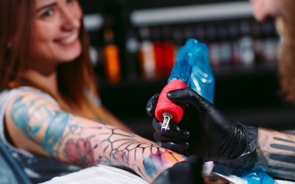 Professionelle Tattoo-Künstler sticht ein Tattoo auf der Hand eines jungen Mädchens im Stil von Wasserfarben.