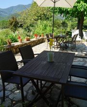 Mesa al aire libre con sombrilla, rodeada de sillas. Jardín verde y montañas al fondo.