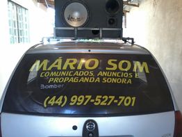 Carro com alto-falante no teto e propaganda "Mário Som" no vidro traseiro com número de contato.