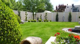 Moderner Garten mit grüner Rasenfläche, dekorativen Pflanzen und einem kleinen Teich.