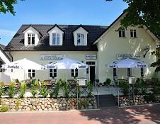 Außenansicht eines Restaurants mit Terrasse, Sonnenschirmen und gepflastertem Weg bei blauem Himmel.