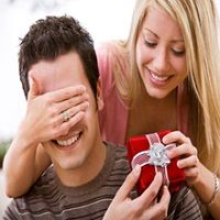 Woman surprises a man with a gift, covering his eyes and holding a red present box.