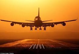 Aereo atterra su pista al tramonto, con cielo arancione intenso.