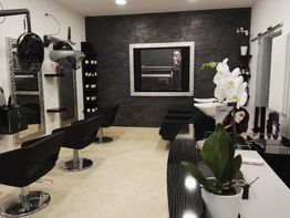 Salone di parrucchiere elegante con poltrone nere, specchi decorati e fiori bianchi sul bancone.