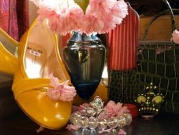 Gelbe Schuhe, rosa Blumen, ein blaues Glas und Schmuck auf einem Tisch arrangiert.