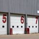 Garage doors numbered 5, 6, and 7 in red on a metal building.
