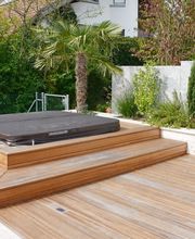 Holzterrasse mit Whirlpool und Garten, umgeben von Pflanzen und einer Mauer im modernen Design.