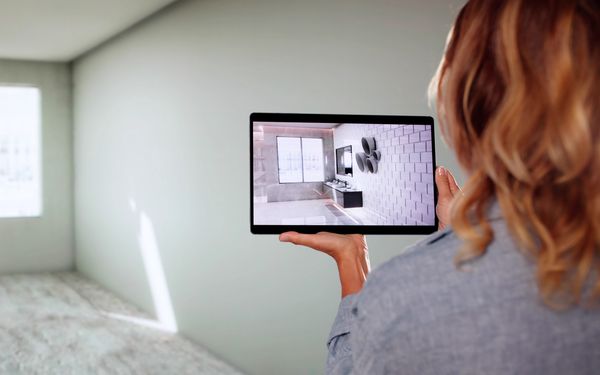 Eine Frau hält ein Tablet auf eine Wand gerichtet, welches ihre gewünschte Sanitäreinrichtung an der Wand zeigt