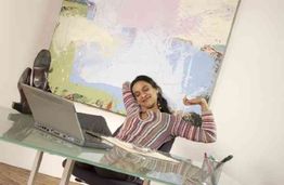 Person lehnt sich entspannt auf einem Stuhl zurück, die Füße auf einem Glas-Schreibtisch.