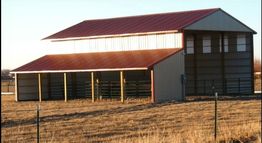 Red-roofed barn on a sunny day, with fences and dry grass surrounding it.