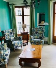 Helles Wohnzimmer mit grüner Wand, gemusterten Sesseln, Holztisch und Balkonblick.