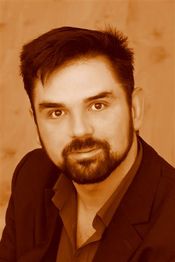 Mann mit Bart und dunklem Haar vor einem hellen Hintergrund in Sepia-Ton.