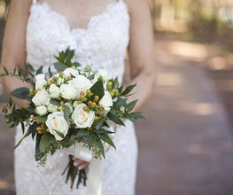 Sposa con abito bianco tiene un bouquet di rose bianche su un sentiero all'aperto.
