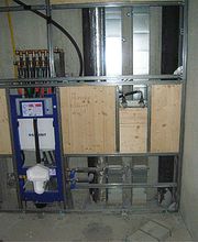 Freiliegende Sanitärinstallation in einem Rohbau mit sichtbaren Rohren und Leitungen.