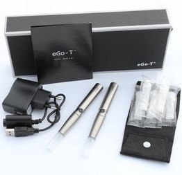 e-Zigaretten-Set mit Ladegerät, zwei Stiften und Zubehör vor schwarzer Verpackung.