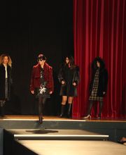 Modelle in schwarzer Kleidung auf einem Laufsteg mit rotem Vorhang im Hintergrund.