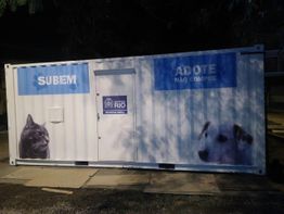 Contêiner branco com imagens de um gato e um cachorro, escrito "SUBEM" e "ADOTE, NÃO COMPRE".