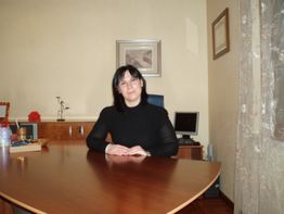 Donna seduta a un tavolo di legno in ufficio, con un computer sullo sfondo.