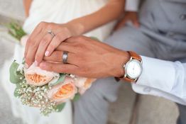 Hands with wedding rings holding a bouquet of roses and baby's breath.