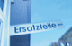 Schild mit der Aufschrift "Ersatzteile" vor blauem Himmel, rechts ein Gebäude.