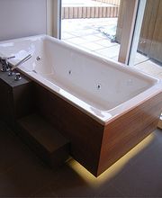 Moderne Badewanne mit Whirlpoolfunktion, Fliesenboden, Holzverkleidung und großem Fenster daneben.