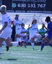 Partido de fútbol femenino, jugadora con balón en primer plano, otras corren en el campo.