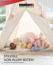 Kind im Zelt mit Kuscheltieren und Flügeln, liegt auf einem Kissen, Fenster im Hintergrund.