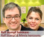 Zwei lächelnde Personen, im Hintergrund helle Wände und Bilder, Text: "Ralf Stumpf Seminare".
