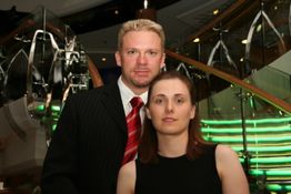 Ein Mann und eine Frau stehen vor einer Treppe, beide sind elegant gekleidet.