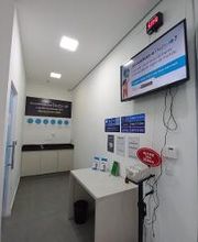 Corredor com mesa, televisão na parede e cartazes informativos em uma clínica ou escritório.