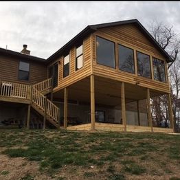 Elevated wooden porch with large windows, supported by posts, attached to a house.