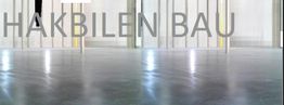 Glänzender Boden vor einem Gebäude mit der Aufschrift „HAKBILEN BAU“.