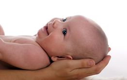 Ein lächelndes Baby liegt in behutsam haltenden Händen, auf weißem Hintergrund.