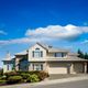 Modern two-story house with a driveway, front garden, and clear blue sky background.