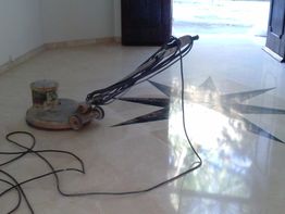 Máquina pulidora sobre suelo de mármol con diseño en estrella y puerta de madera abierta.