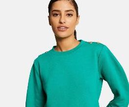Mujer con jersey verde y cabello recogido, posa con fondo blanco.