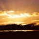 Sonnenuntergang über einem See mit reflektierendem Wasser und Wolken am Himmel.