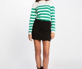 Mujer con suéter de rayas verdes y falda negra, posando con botas negras.