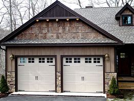 A rustic-style house with two beige garage doors and stone accents, set in a wooded area.