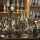 Intricately designed metal vases and jugs on display with a blurred background on wooden shelves.