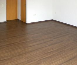 Leerer Raum mit braunem Holzboden und zwei Holztüren an der linken Wand.