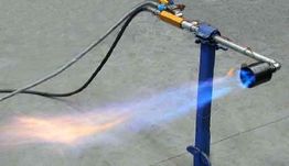 Bruciatore a gas acceso su un supporto blu con fiamma blu e arancione su sfondo grigio.