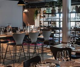 Elegantes Restaurant mit gedeckten Tischen, modernen Stühlen und Regalen im Hintergrund.